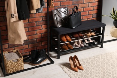 Photo of Stylish hallway with shoe storage bench and accessories near brick wall. Interior design