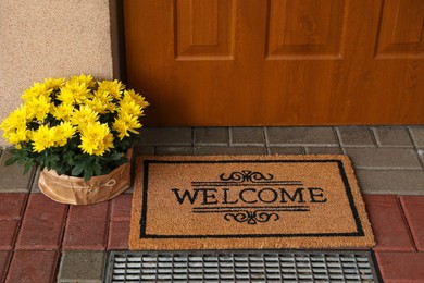 Door mat with word Welcome and beautiful flowers near entrance