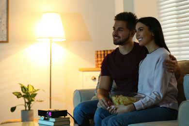 Young couple watching movie using video projector at home. Space for text