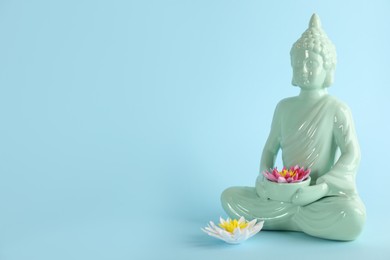 Beautiful ceramic Buddha sculpture with flowers on light blue background. Space for text