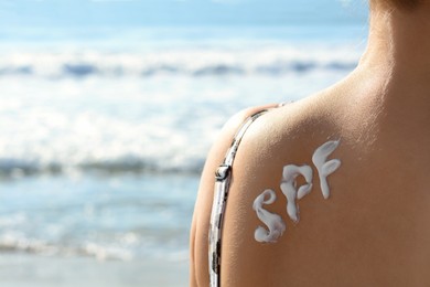 Photo of Woman with sun protection cream on her back at beach, closeup. Space for text