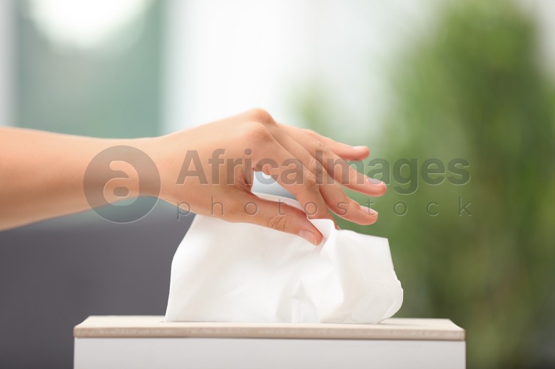 Woman taking paper tissue from holder on blurred background, closeup