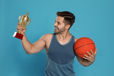 Portrait of happy young basketball player with gold trophy cup on blue background