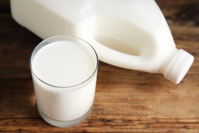 Glass of milk near gallon bottle on wooden table, closeup