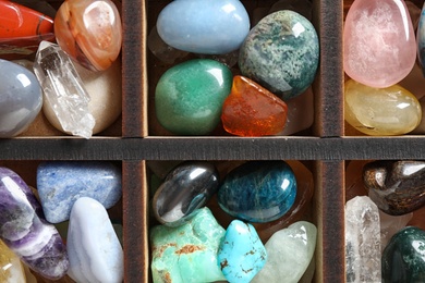 Box with different beautiful gemstones as background, top view