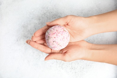 Photo of Woman holding color bath bomb over foam, top view