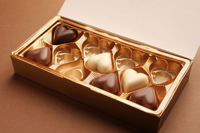 Photo of Partially empty box of chocolate candies on brown background, closeup