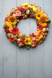 Beautiful autumnal wreath with flowers, berries and fruits on light grey wooden background, top view. Space for text