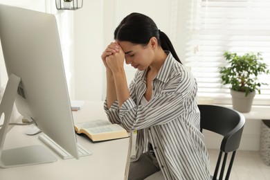 Beautiful young woman praying over Bible at desk