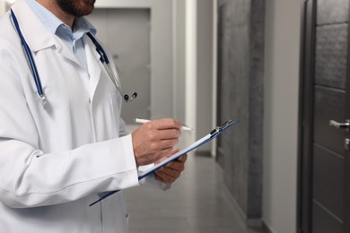 Doctor in white coat with stethoscope and clipboard indoors, closeup. Space for text