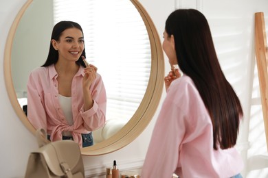 Photo of Young woman doing makeup near mirror at home. Morning routine
