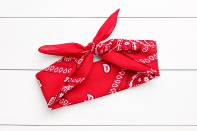 Tied red bandana with paisley pattern on white wooden table, top view