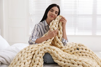 Photo of Young woman with chunky knit blanket on bed at home