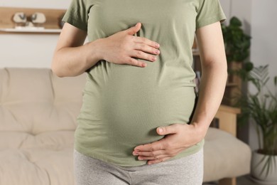 Photo of Pregnant woman touching belly in living room, closeup