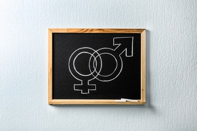 Small blackboard with drawn gender symbols on white wall. Sex education