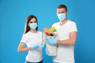 Volunteers in protective masks and gloves with products on blue background. Aid during coronavirus quarantine
