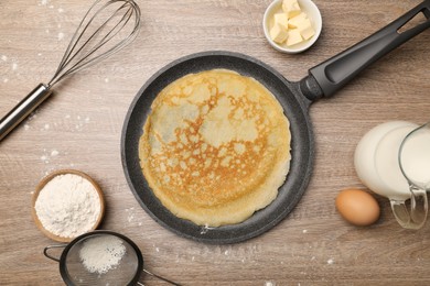 Photo of Frying pan with delicious crepe and ingredients on wooden table, flat lay
