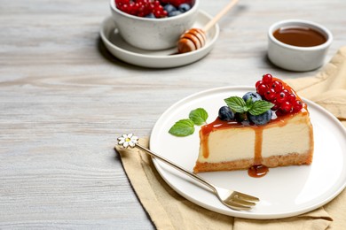 Photo of Slice of delicious cheesecake served with berries and caramel sauce on white wooden table, space for text