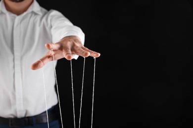 Photo of Man in formal outfit pulling strings of puppet on black background, closeup. Space for text