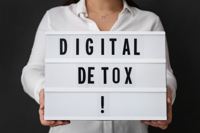 Photo of Woman holding lightbox with phrase DIGITAL DETOX on black background, closeup