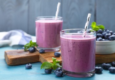 Photo of Glasses of blueberry smoothie with mint and fresh berries on turquoise wooden table, space for text