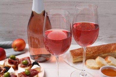 Photo of Delicious rose wine and snacks on white table, closeup