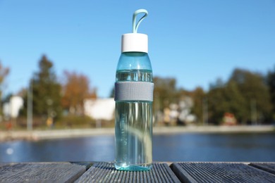 Glass bottle with water on wooden pier near river outdoors