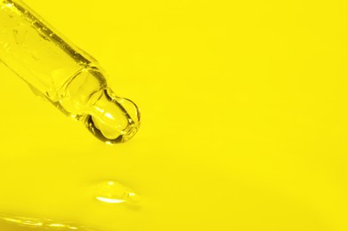 Dripping face serum from pipette on yellow background, closeup. Space for text