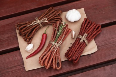 Photo of Bundles of delicious kabanosy with rosemary, peppercorn, garlic and chilli on wooden table, above view