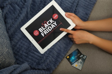 Woman with credit cards using tablet for online shopping on sofa, top view. Black Friday sale