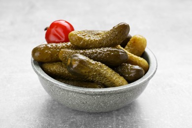 Bowl of pickled cucumbers and pepper on light grey table, closeup