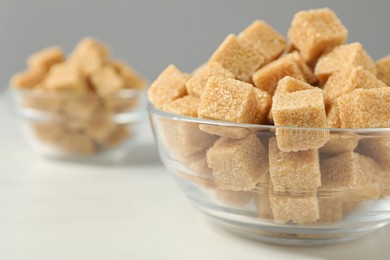 Brown sugar cubes in glass bowl on white table, closeup. Space for text
