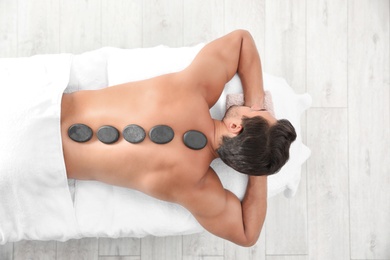 Young man receiving hot stone massage in spa salon, top view. Space for text