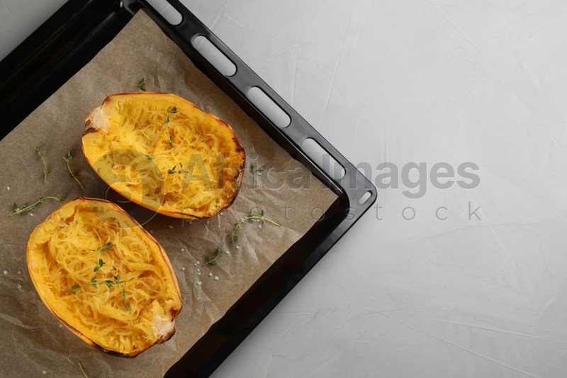 Baking sheet with halves of cooked spaghetti squash and thyme on light grey table, top view. Space for text