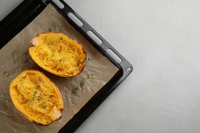 Baking sheet with halves of cooked spaghetti squash and thyme on light grey table, top view. Space for text