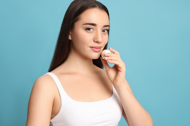 Young woman applying lip balm on turquoise background
