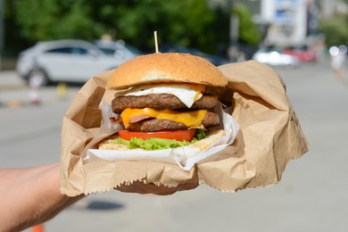 Photo of Woman holding delicious burger in paper wrap on city street, closeup