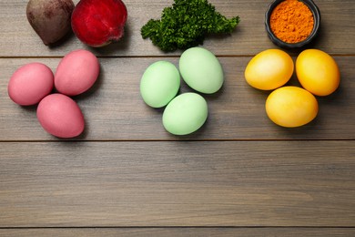 Photo of Colorful Easter eggs painted with natural dyes and ingredients on wooden table, flat lay. Space for text