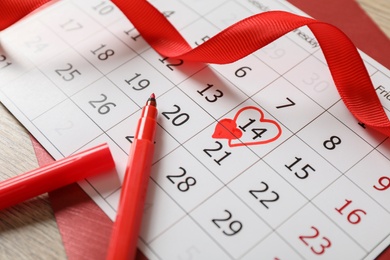 Calendar with marked Valentine's Day, red ribbon and marker on wooden table, closeup