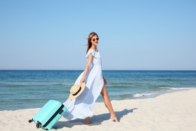 Beautiful woman with suitcase on sandy beach near sea