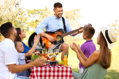 Man playing guitar for friends at picnic in park
