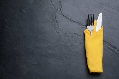 Shiny fork and knife with napkin on black table, top view. Space for text