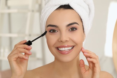 Photo of Beautiful young woman applying mascara in bathroom at home