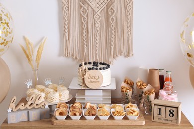 Baby shower party. Different delicious treats on wooden table and decor near light wall
