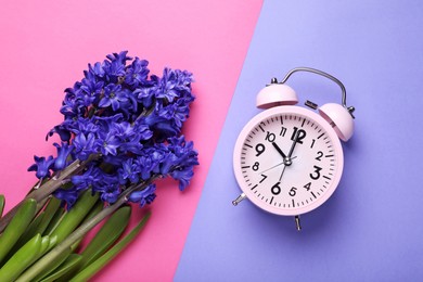 Photo of Pink alarm clock and beautiful hyacinth flowers on color background, flat lay. Spring time