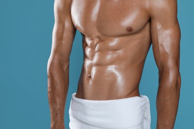 Shirtless man with slim body and towel wrapped around his hips on light blue background, closeup