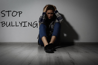 Message STOP BULLYING and abused teen girl crying near white wall
