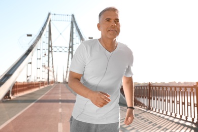 Photo of Handsome mature man running on bridge, space for text. Healthy lifestyle