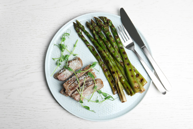 Tasty meat served with grilled asparagus on white wooden table, top view