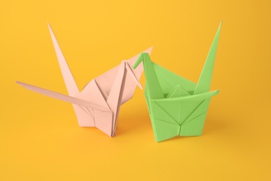 Photo of Origami art. Beautiful light green and pale pink paper cranes on orange background